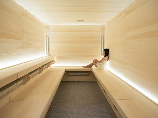 A woman sitting inside a a well lit commercial infrared sauna
