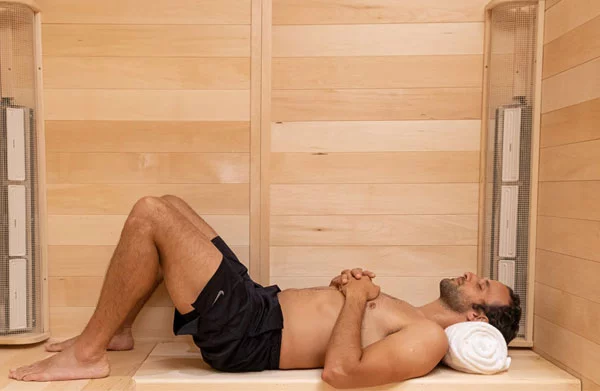 A man lying down inside a 3 person infrared sauna made by SaunaRay
