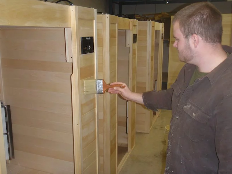 a man brushing on a coat of beeswax finish to a newly constructed SaunaRay far infrared sauna
